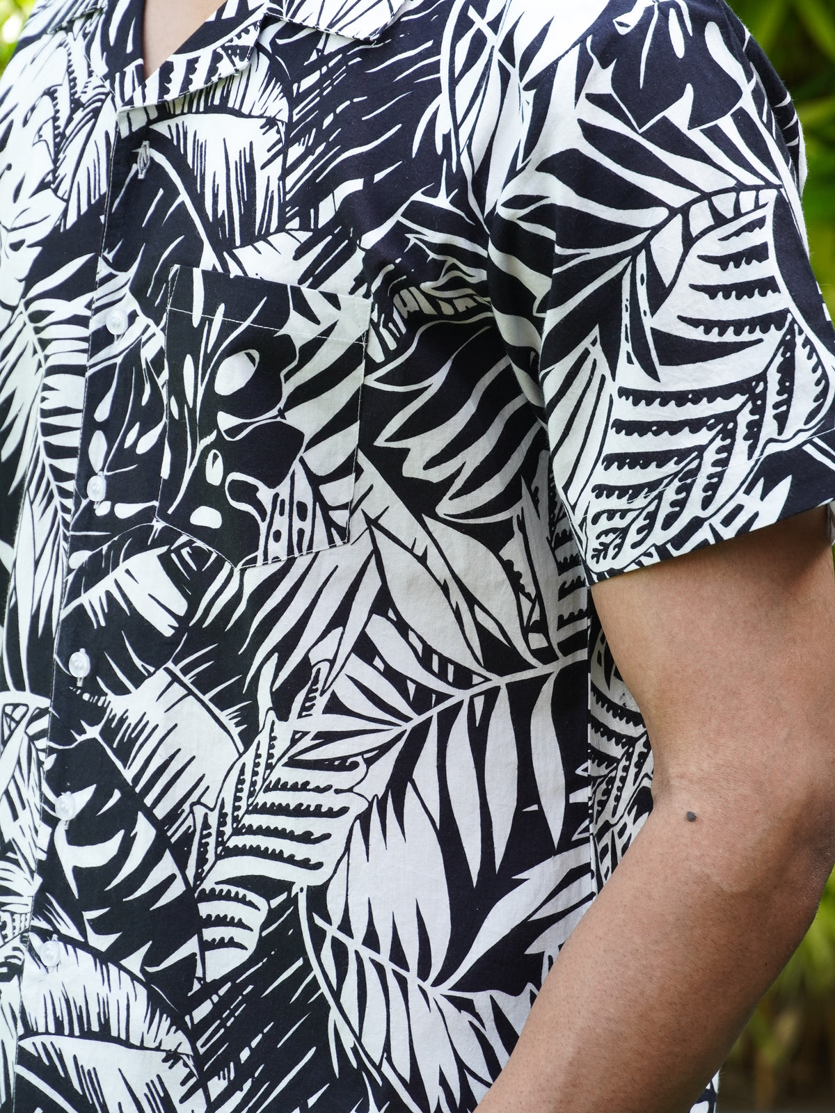 Close-up of white tropical leaf and palm foliage print on black cotton shirt