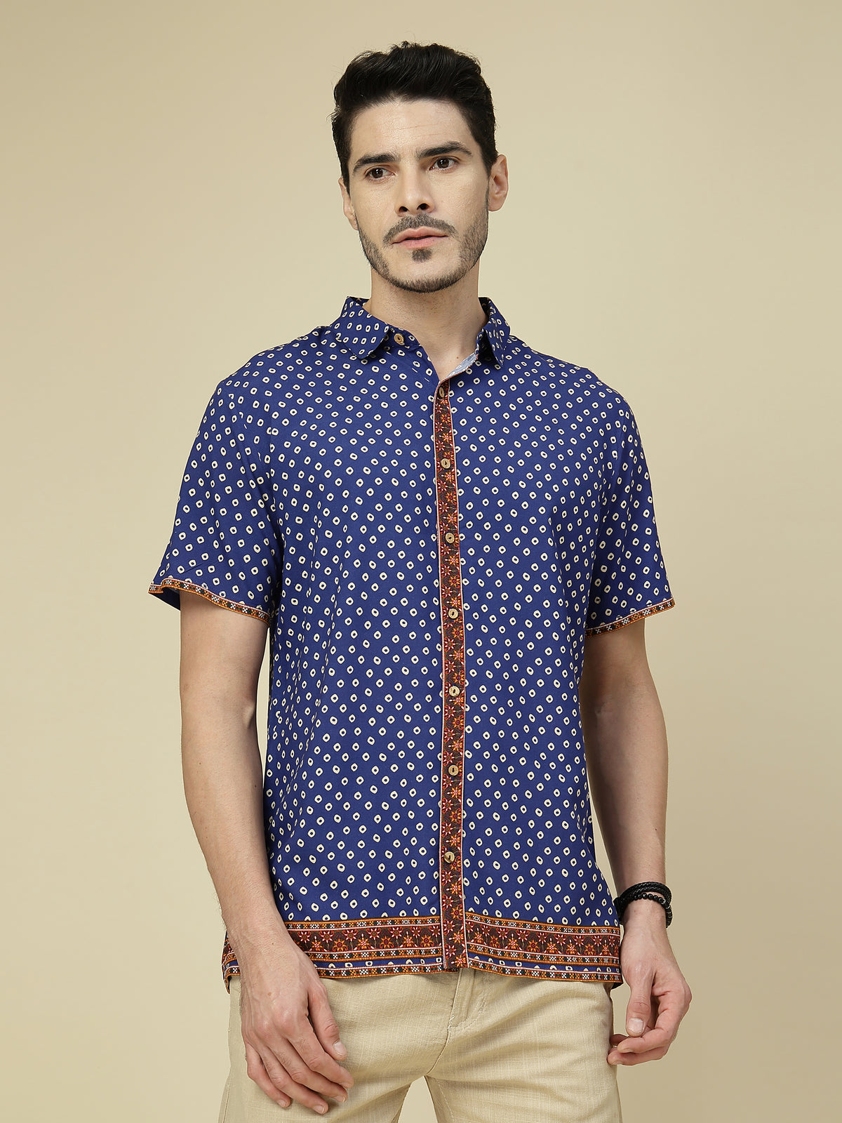 Model wearing a blue geometric half sleeve shirt with rust-red borders and beige trousers